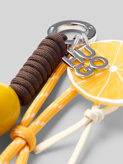 Produktfoto, Schlüsselanhänger mit Zitrone-Applikation Modell 'BECKY_CHARM' von HUGO, mehrfarbig mit Kordeln, Gummi-Perlen und Metall-Logo, Material Zink, Detailaufnahme.