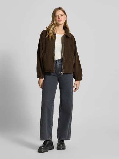 Modelka nosi kurtkę Teddyfell-Jacke mit Zweiwege-Reißverschluss Modell 'ENNA' od Pegador, futerko, krój relaxed fit, wykładany kołnierz, wpuszczane kieszenie, długość tyłu w rozmiarze S: 53 cm, szerokość ramion w rozmiarze S: 46 cm, szerokość klatki piersiowej w rozmiarze S: 53 cm, długość rękawów w rozmiarze S: 62 cm; brązowe odcienie, miękka tekstura, luźny krój. Pełny widok z przodu.