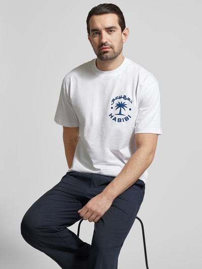 Męski model nosi Regular Fit T-Shirt aus reiner Baumwolle Modell 'KARAN' od Strellson, biały z granatowym nadrukiem, krój regular fit, okrągły dekolt, krótki rękaw, unikatowa tekstura bawełny, widok z przodu, ujęcie górnej połowy ciała.