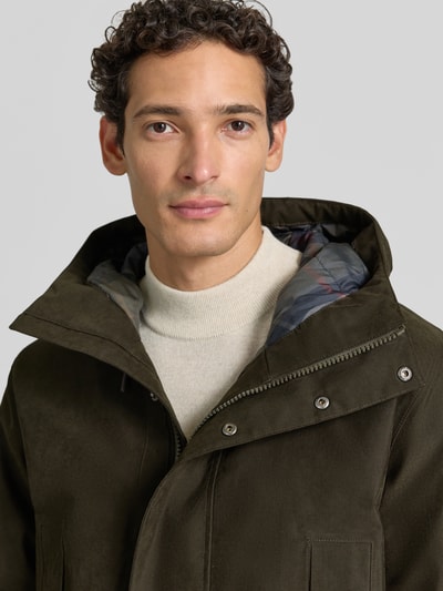 Männermodel trägt Regular Fit Funktionsjacke mit Kapuze von Barbour in Oliv, glatte Textur, Kontrastfutter, Nahaufnahme Oberkörper.