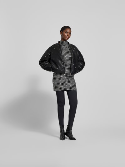 Frauenmodel trägt Jacke mit Stehkragen von ROTATE in Leder-Optik mit Ziersteinbesatz, Regular-Fit, schwarz, Ganzkörperansicht von vorne. Rückenlänge 57 cm, Brustweite 51 cm, Ärmellänge 65 cm bei Größe 36. Reißverschluss.