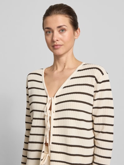 Modelka nosi Loose Fit Cardigan aus Viskose-Mix Modell 'NURIA' od VILLA SOPHIE, efekt: wzór na całej powierzchni, taśma do wiązania, dekolt w serek, aplikacja z metką, długi rękaw, dzianina, mieszanka wiskozy, jasnobeżowe i czarne paski, faktura prążkowana, zbliżenie na górną część ciała