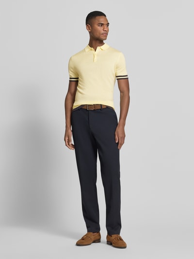 Męski model nosi Slim Fit Poloshirt aus Lyocell-Seide-Mix od Guess, żółty z kontrastowym paskiem, krój slim fit, widok całej sylwetki z przodu.