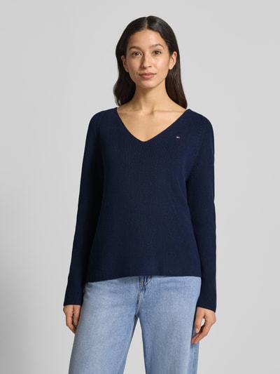 Kobiece modelka nosi Regular Fit Sweter z dzianiny z czystej bawełny od Tommy Hilfiger, efekt: jednolity kolor, wzór w paski, wyhaftowane logo, dekolt w serek, długi rękaw, raglanowe rękawy, prążkowana dzianina, kolor granatowy, widok na cały korpus z przodu.