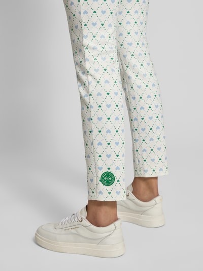 Frauenmodel trägt Slim Fit Stoffhose mit Allover-Logo-Print von Marc Cain aus Elastischer-Material-Mix, geometrisches Muster, helle Farben, Nahaufnahme Bein.