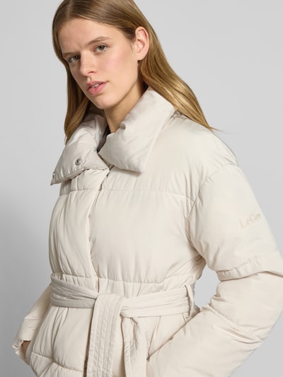 Frauenmodel trägt Steppjacke mit Bindegürtel Modell 'Margitta' von LeGer by Lena Gercke in Beige mit Stehkragen, Eingrifftaschen, Nahaufnahme Oberkörper. Rückenlänge 70 cm, Schulterbreite 57 cm, Brustweite 58 cm, Ärmellänge 55 cm bei Größe 36, Regular-Fit, glatte strukturierte Oberfläche.