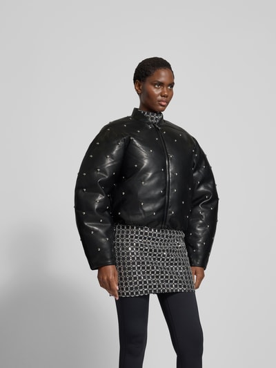Frauenmodel trägt Jacke mit Stehkragen von ROTATE, Regular Fit, schwarze Leder-Optik mit Ziersteinbesatz, Reißverschluss, Ganzkörperansicht von vorne.