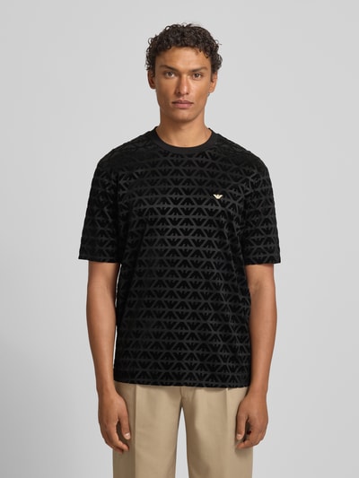 Männermodel trägt T-Shirt mit Label-Stitching von Emporio Armani, schwarz gemustert, Lyocell-Baumwoll-Mix, Regular-Fit, Ganzkörperansicht von vorne.
