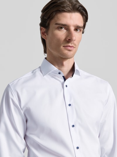Mężczyznamodel nosi Regular Fit Businesshemd aus Baumwolle mit Kentkragen od ETERNA, biała bawełna, kołnierzyk kent, krój regular fit, listwa guzikowa, długość tyłu w rozmiarze 40: 74 cm, szerokość ramion w rozmiarze 40: 46 cm, długość rękawa w rozmiarze 40: 65 cm, zbliżenie na górną część ciała