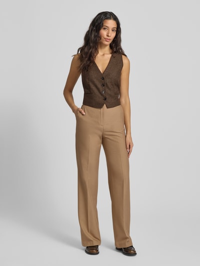 Frauenmodel trägt Regular Fit Weste mit V-Ausschnitt Modell 'PIPER' von Mango in Braun, kombiniert mit beigefarbener Hose, Ganzkörperansicht von vorne. Damenweste mit Paspeltaschen, Knopfleiste, Rückenlänge 44 cm, Schulterbreite 30 cm, Brustweite 31 cm, texturierte Optik.