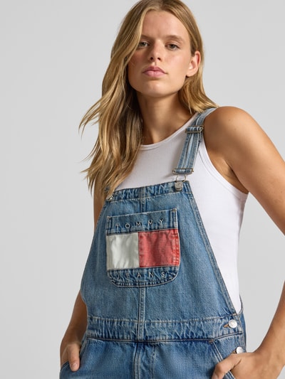 Frauenmodel trägt Relaxed Fit Latzhose aus reiner Baumwolle von Tommy Jeans, blaue Denim-Textur mit Logo-Details, Nahaufnahme Oberkörper, Damen Latzhose von Tommy Jeans