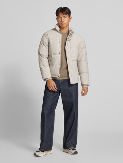 Männermodel trägt gewatteerd jack met opstaande kraag Model 'SOHO' van JACK & JONES, regular fit, ruglengte maat M 70 cm, schouderbreedte 47 cm, borstwijdte 60 cm, mouwlengte 68 cm, lichtbeige kleur, gladde textuur, knoop- en ritssluiting, rechte vormen, Ganzkörperansicht van voren.