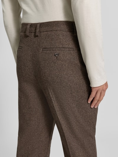 Męski model nosi Straight Fit Stoffhose mit Baumwoll-Anteil od Lindbergh w kolorze brązowym, elastyczna mieszanka materiałów, zapięcie na guzik i zamek błyskawiczny, wpuszczane kieszenie oraz kieszenie z tyłu, kontrafałda, szerokość w rozmiarze M: 41 cm, długość wewnętrzna nogawki w rozmiarze M: 80 cm, ujęcie z tyłu zbliżenie na biodra