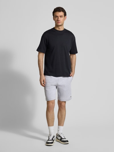 Męski model nosi Regular Fit Sweatshorts aus Baumwoll-Mix od Lacoste w kolorze jasnoszarym, krój regular fit, bawełniany materiał, naszywka z logo, elastyczny pas ze sznurkiem do regulacji, boczne kieszenie, tylnia kieszeń, widok całej sylwetki z przodu.