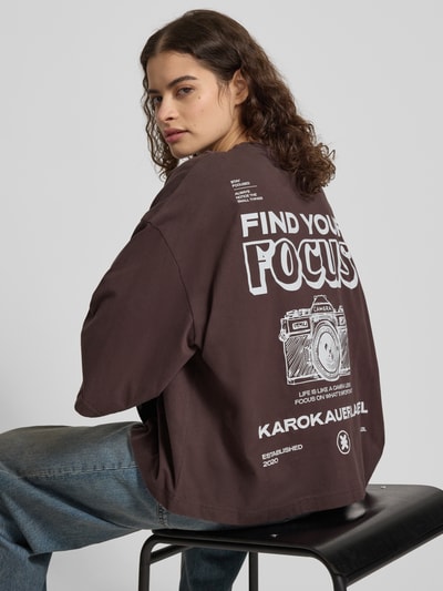 Kobiece model nosi Oversized T-Shirt mit Rundhalsausschnitt od Karo Kauer z bawełny, krój oversized, nadruk z logo, okrągły dekolt, długość tyłu 59 cm, ujęcie z tyłu