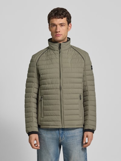Männermodel trägt Steppjacke mit Stehkragen und Reißverschlusstaschen von NAUTGÅRD in khaki, Regular-Fit, Ganzkörperansicht von vorne. Kontext: Rückenlänge bei Größe M 69 cm, Schulterbreite 40 cm, Brustweite 46 cm, Ärmellänge 62 cm.
