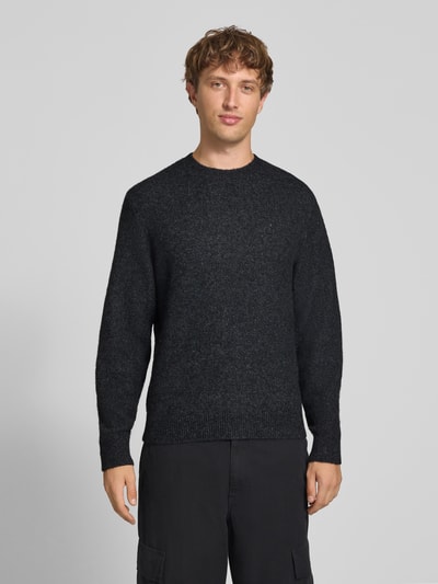 Männermodel trägt Strickpullover mit Logo-Stitching Modell 'CURTIS' von Carhartt Work In Progress, dunkle Farbe, lockerer Schnitt, Ganzkörperansicht von vorne.