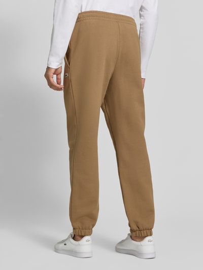 Männermodel trägt Regular Fit Sweathose aus Baumwoll-Mix von Lacoste in Hellbraun, elastische Bündchen, glatte Textur, Ganzkörperansicht Rückansicht. Herren Sweathose von Lacoste