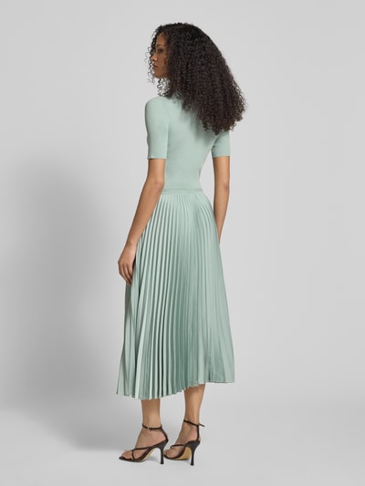 Vrouwenmodel draagt Regular Fit Businesskleid uit verschillende materialen model 'FADRIDI' van BOSS, effen kleuren, midilengte, ronde hals, korte mouw, plissérok van satijn, ribtricot materiaalverwerking, geheellichaamsaanzicht achteraan