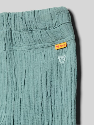 Produktfoto, grünblaue Hose mit Eingrifftaschen und Stitching von Steiff, reine Baumwolle, Label-Detail, elastischer Bund mit Tunnelzug, strukturierte Oberfläche.