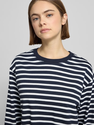 Kobieta nosi Loose Fit Langarmshirt aus reiner Baumwolle od Marc O'Polo Denim, efekt: jednolity kolor, wzór w paski, okrągły dekolt, bawełna, aplikacja z wyhaftowanym logo, bluzka z długim rękawem; zbliżenie na górną część ciała.