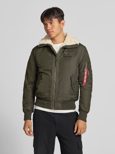 Männermodel trägt Bomberjacke mit Label-Patch und Kentkragen von Alpha Industries in Olivgrün, Teddyfellkragen, Ganzkörperansicht von vorne. Regular Fit, Reißverschluss, gerippte Abschlüsse, Reißverschlusstasche und Eingrifftaschen, Brustweite 56 cm bei Größe M.