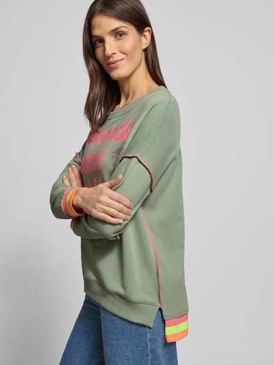 Modelka nosi Oversized Sweatshirt mit gerippten Abschlüssen od miss goodlife z bawełny, krój oversized, prążkowane wykończenia, okrągły dekolt, nadruk z napisem. Ujęcie całej sylwetki z przodu.