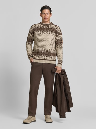 Männermodel trägt Regular Fit Pullover aus reiner Wolle Modell 'Albertville' von Dale of Norway, Strick-Optik, beige-braune Muster, Ganzkörperansicht von vorne. Rückenlänge bei Größe M 66 cm, Ärmellänge 59 cm.