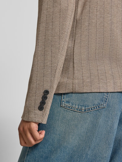 Frauenmodel trägt Blazer mit Viskose-Anteil Modell 'Bonnie' von FREE/QUENT, beige mit Fischgrätmuster, glatte Textur, Detailaufnahme Ärmel. Elastischer Material-Mix, eng anliegende Passform, Reverskragen.