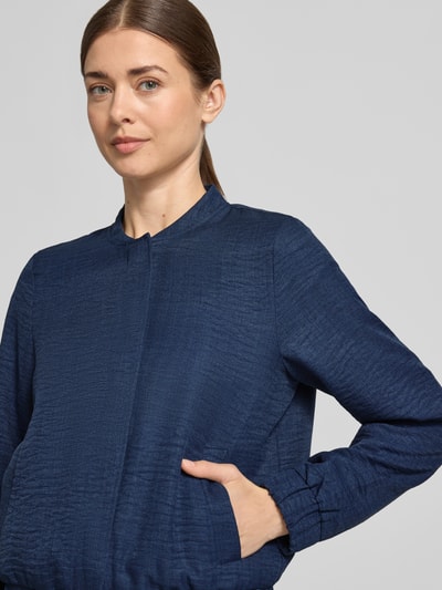 Modelka kobieca nosi Regular Fit Blouson mit Baseball-Kragen Modell 'MELANEY' od Vero Moda, kolor melanżowy, z długim rękawem, boczne kieszenie, struktura materiału widoczna, krój regular fit, z zapięciem na ukryte napy, z mankietami i dołem z prążkowanym wykończeniem, zbliżenie na górną część ciała, widok z przodu.
