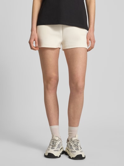 Frauenmodel trägt Shorts mit Kordelzug und Logo-Print Modell 'BRITNEY' von Guess Activewear, Cremefarbe, Baumwoll-Mix, Loose Fit, Ganzkörperansicht von vorne.