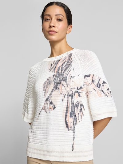 Frauenmodel trägt Strickshirt mit Rundhalsausschnitt von Marc Cain, cremefarben mit Strukturmuster und floralem Allover-Look, Ganzkörperansicht von vorne. Baumwoll-Mix mit Viskose-Anteil, Regular Fit, 1/2-Arm, Rückenlänge 51 cm, Ärmellänge 24 cm.