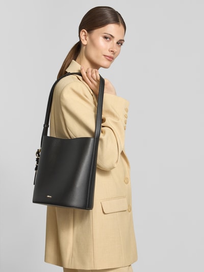 Kobiece model nosi torebka typu bucket bag Bucket Bag mit Logo-Applikation Modell 'Roxie' od Furla w kolorze czarnym, z główną przegrodą z zapięciem na magnes, regulowanym paskiem na ramię, aplikacją z logo, przegródką zapinaną na zamek błyskawiczny wewnątrz, szerokość w rozmiarze 1: 24 cm, długość w rozmiarze 1: 26 cm, głębokość w rozmiarze 1: 17 cm, długość paska na ramię w rozmiarze 1: 67 cm, całe zdjęcie górnej połowy z przodu.