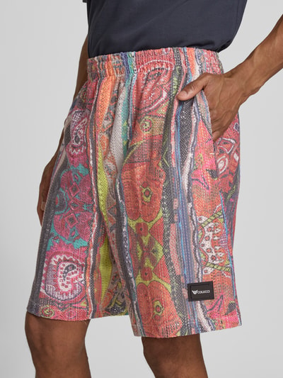 Männermodel trägt Straight Fit Shorts in Crochet-Optik mit Viskose-Anteil von COLUCCI, bunt, elastischer Bund, Logo-Detail, Nahaufnahme Oberschenkel.