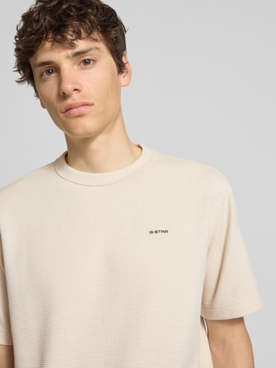 Männermodel trägt Regular Fit T-Shirt mit Strukturmuster von G-Star Raw in Beige, Rundhalsausschnitt, Logo, Nahaufnahme Oberkörper. Herren T-Shirt, Rückenlänge bei Größe M: 71 cm.