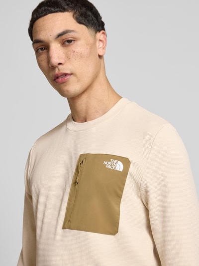 Männermodel trägt bluzka z długim rękawem z elastyczna mieszanka materiałów model 'KECHA' od The North Face z prosty krój, okrągły dekolt, napoleońska kieszeń i detal z logo, długość tyłu w rozmiarze M: 67 cm, kolor beżowy z kontrastującą kieszenią, struktura siateczkowa, zbliżenie na górną część ciała, zdjęcie frontralne