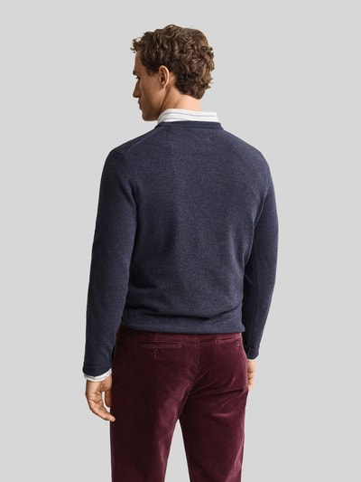 Männermodel trägt Regular Fit Pullover aus reiner Wolle von GANT in Dunkelblau, kombiniert mit bordeauxroser Hose, Ganzkörperansicht Rückansicht.