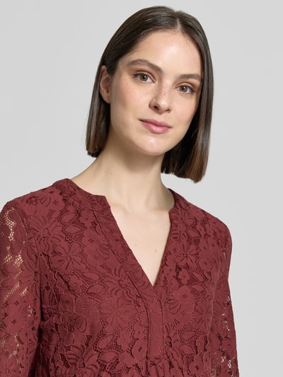 Modelka kobieca nosi Loose Fit Spitzenkleid aus Baumwoll-Mix Modell 'HONEY' od Vero Moda w kolorze bordowym, wzór koronkowy, dekolt V, długość do kolan, rękaw 3/4 z dzwonkowatym mankietem, materiał bawełniany. Zbliżenie na górną część ciała.