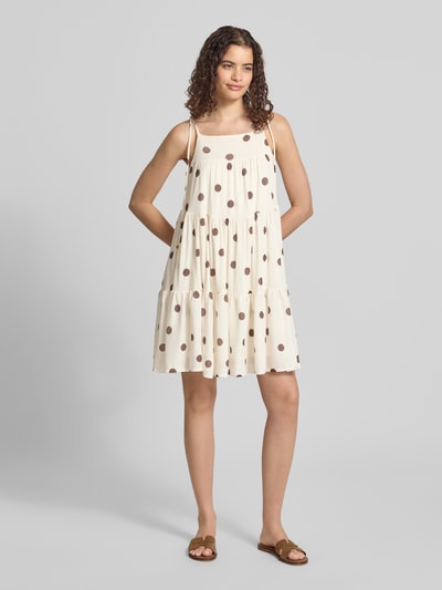 Frauenmodel trägt Minikleid im Stufen-Look Modell 'Flowy' von Gina Tricot, A-Linie, Allover-Look, creme mit braunen Punkten, Ganzkörperansicht von vorne.
