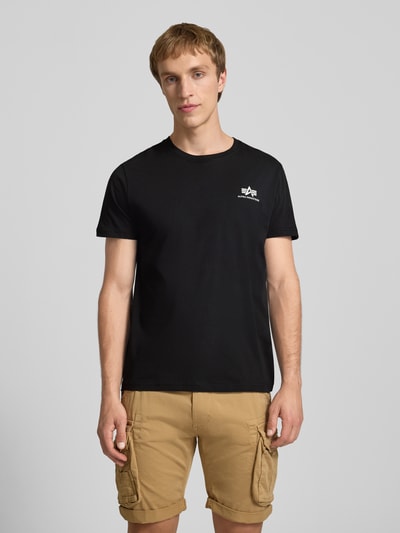 Männermodel trägt T-Shirt mit Logo und Rundhalsausschnitt von Alpha Industries, reine Baumwolle, Regular-Fit, schwarze Farbe, Ganzkörperansicht von vorne. Rückenlänge in Größe M: 67 cm.