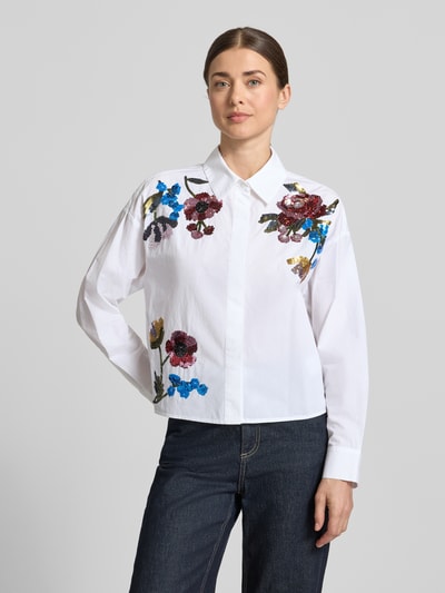 Modelka kobieca nosi Boxy Fit Bluse mit Pailletten od Oui z czystej bawełny, białe tło, kolorowe cekiny, kołnierz koszulowy, ukryta lista guzikowa, długość tyłu 55 cm, długość rękawa 52 cm; widok całej sylwetki z przodu.