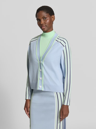 Frauenmodel trägt Strickjacke aus Lyocell-Mix mit Knopfleiste von Marc Cain in Pastellblau mit Kontraststreifen und geripptem Bund, lockere Passform, Oberteil mit durchgehender Knopfleiste, überschnittene Schultern, Nahaufnahme Oberkörper.
