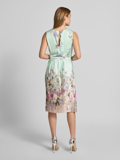 Frauenmodel trägt Knielanges Cocktailkleid mit Plisseefalten von Rinascimento, A-Linie, Material-Mix, florales Mintgrün, Ganzkörperansicht Rückansicht.