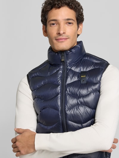 Männermodel trägt dunkelblaue Steppweste mit Zweiwege-Reißverschluss Modell 'DANNY' von Blauer USA, glatte Struktur, Nahaufnahme Oberkörper, Regular Fit, sichtbarer Stehkragen, KI-modifiziertes Bild.