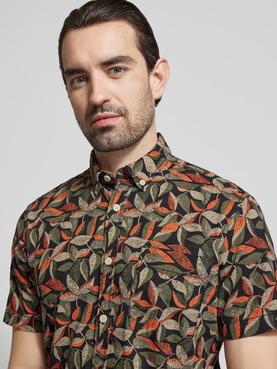 Männermodel trägt Regular Fit Freizeithemd aus reiner Baumwolle von camel active mit Blätterprint in Schwarz, Orange und Beige, Nahaufnahme Oberkörper.