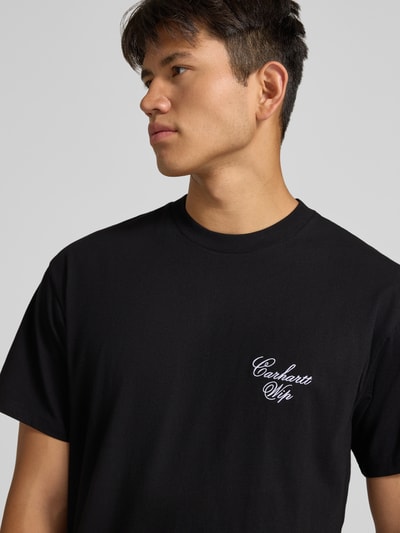 Männermodel trägt schwarzes T-Shirt mit Logo-Stitching Modell 'Gracious' von Carhartt Work In Progress, reine Baumwolle, Nahaufnahme Oberkörper.