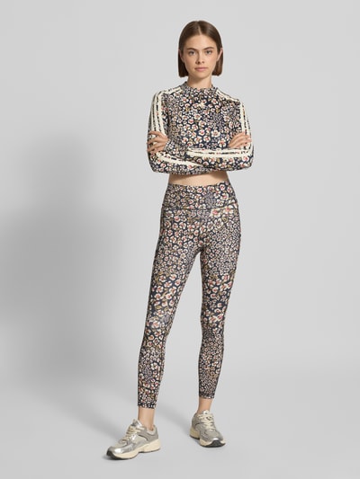 Frauenmodel trägt Slim Fit Sport-Leggings mit floralem Muster Modell 'FARM LEGGINGS' von adidas Sportswear, Ganzkörperansicht von vorne.