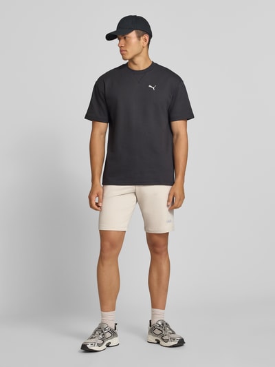 Männermodel trägt Shorts mit Logo und elastischem Bund von PUMA im Baumwoll-Mix, Regular Fit, Beige, Ganzkörperansicht von vorne. Kontext: Herren Shorts von PUMA Performance, Logo, elastischer Bund, Bundweite bei Größe M: 39 cm, Innenbeinlänge bei Größe M: 26 cm.