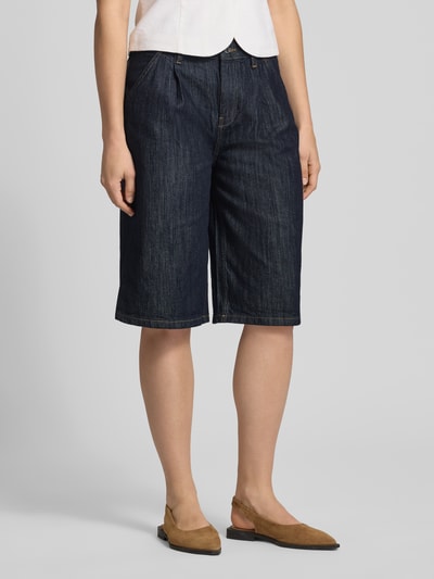 Kobiece model nosi Long Shorts mit Eingrifftaschen od Gina Tricot, mieszanka bawełny z dodatkiem streczu, krój loose fit, zapięcie na guzik i zamek błyskawiczny, wpuszczane kieszenie boczne, kieszenie z tyłu, szerokość w rozmiarze 36: 42 cm, długość wewnętrzna nogawki w rozmiarze 36: 31 cm, ciemnoniebieski denim, wyraźna tekstura, całkowity widok z przodu
