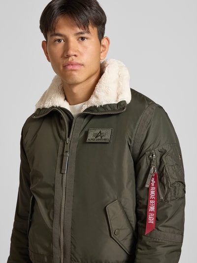 Männermodel trägt Bomberjacke mit Label-Patch und Kentkragen von Alpha Industries in Olivgrün mit Teddyfell, Nahaufnahme Oberkörper. Herren Bomberjacke, Regular Fit, Reißverschluss, Reißverschlusstasche am Ärmel mit Label-Patch, Eingrifftaschen mit Druckknopfverschluss, gerippte Abschlüsse, Rückenlänge 65 cm, Schulterbreite 45 cm, Brustweite 56 cm, Ärmellänge 65 cm.